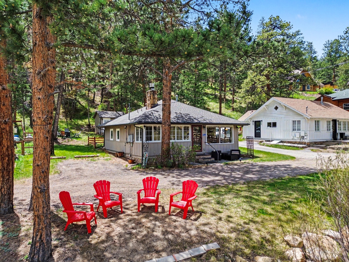 Charming cabin nestled among tall pines with vibrant red Adirondack chairs so you can sit and listen to the river.