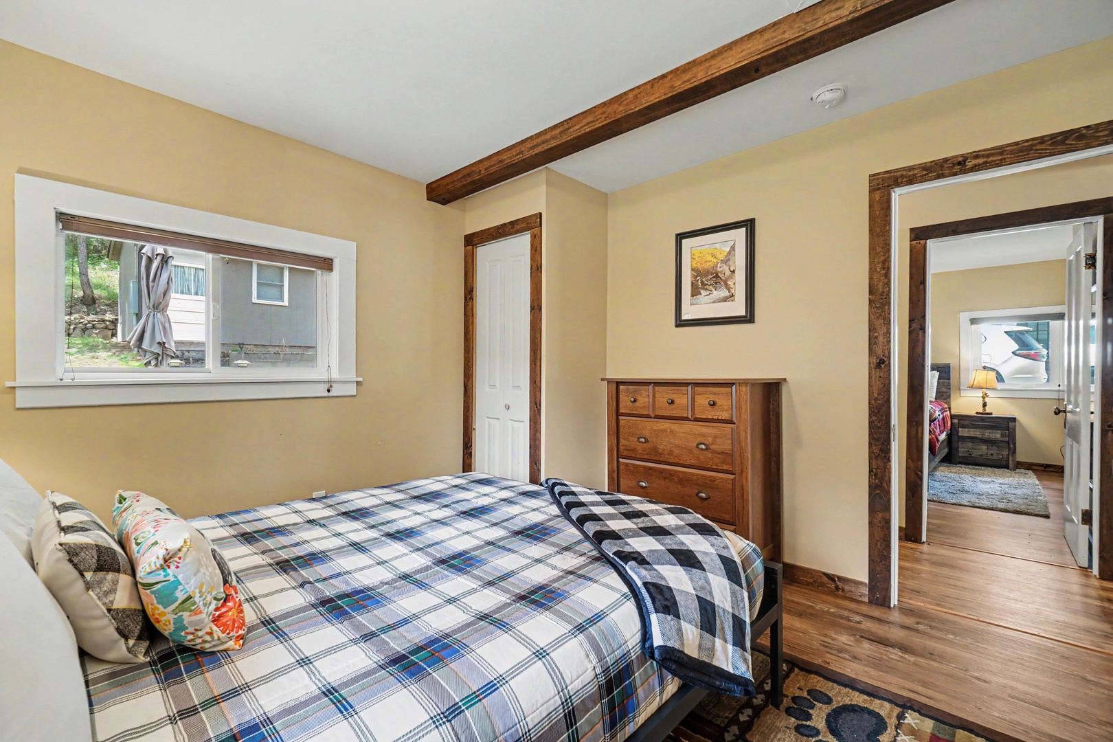 Your cozy bedroom features rustic wood beams, warm hardwood floors, and a plush bed dressed in cheerful plaid linens—perfect for restful nights after your adventures.