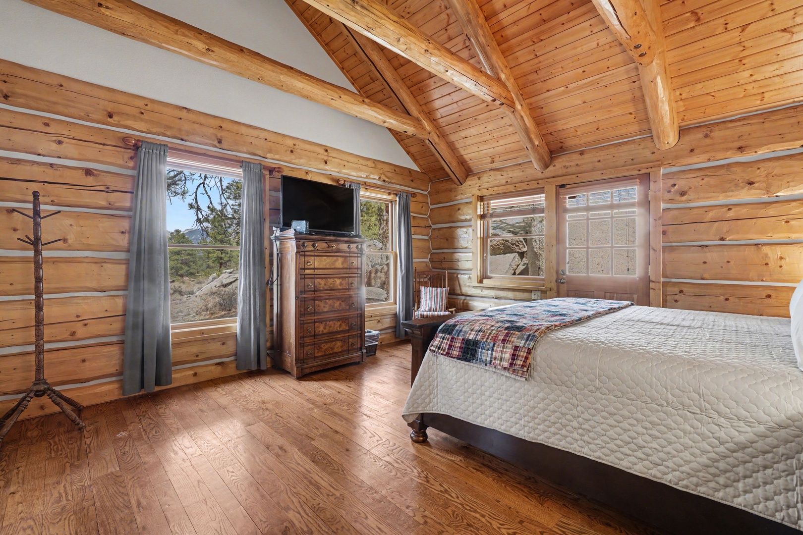 Wake up in your rustic log cabin bedroom with soaring beams, natural wood warmth, and peaceful mountain views through panoramic windows.