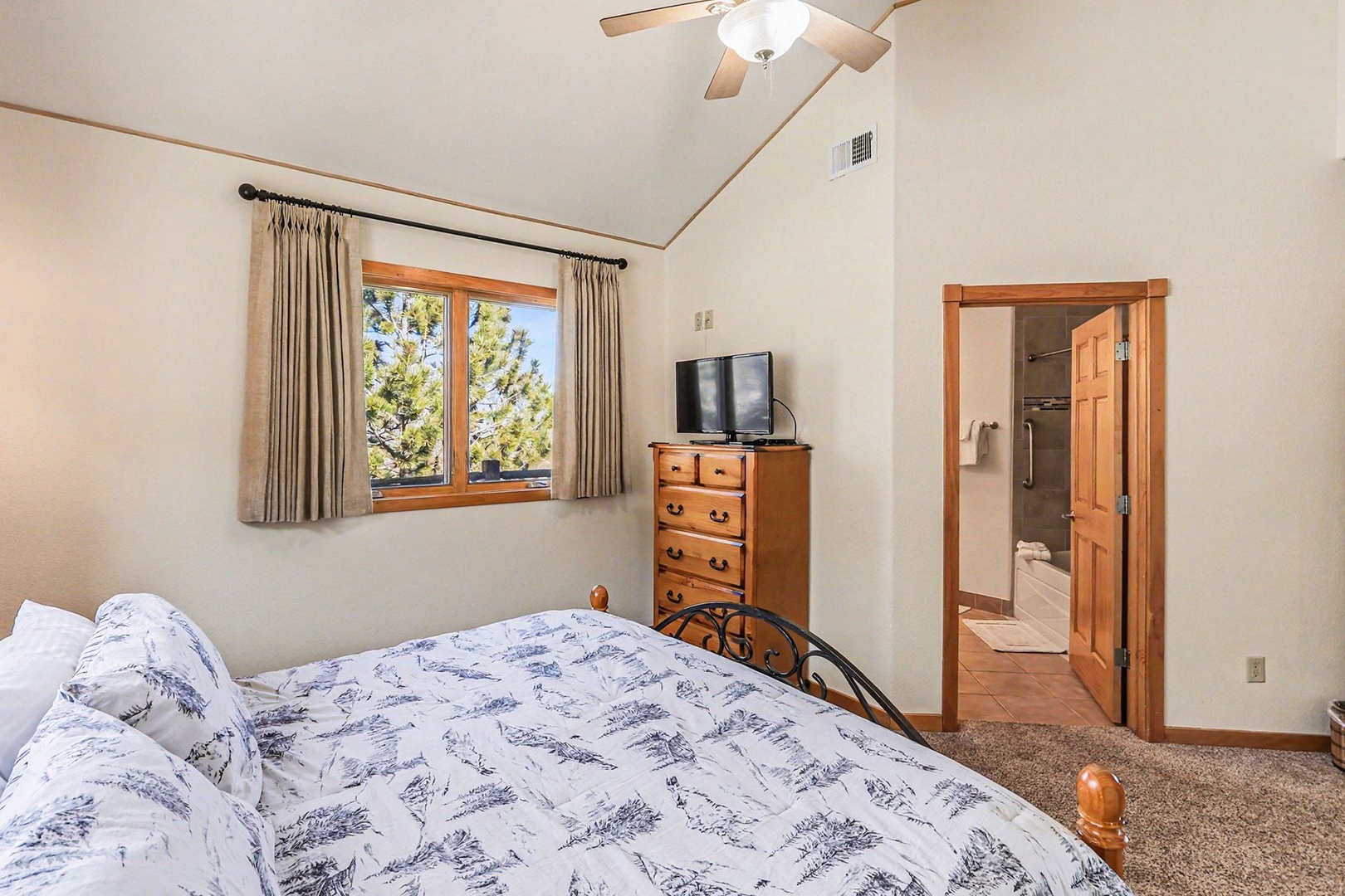 Rest peacefully in your serene king bedroom with vaulted ceilings, warm wood accents, and treetop views through charming windows.