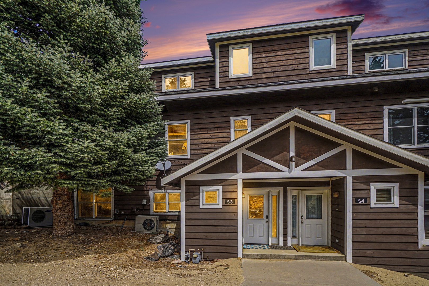 Modern wooden townhome with warm evening glow illuminating the windows, creating a welcoming atmosphere against the beautiful sunset sky.