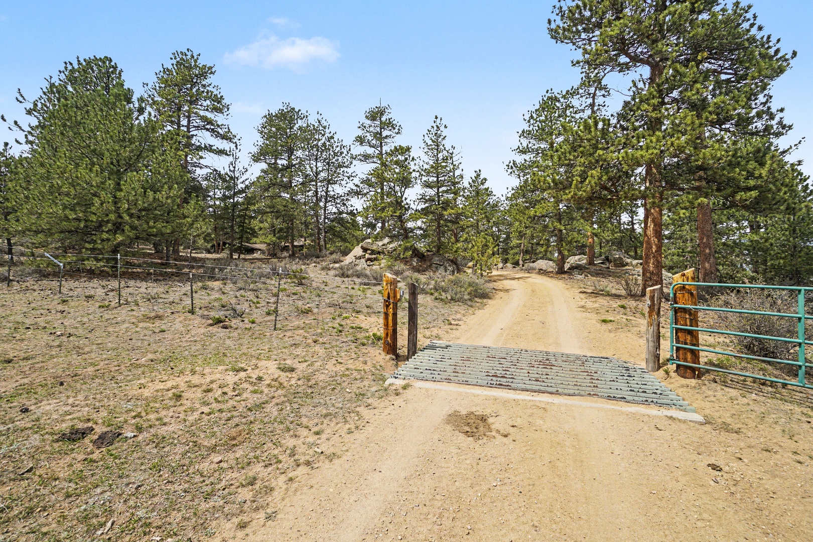Entrance gate opens to a scenic dirt road winding through pine forest toward the mountain retreat property.