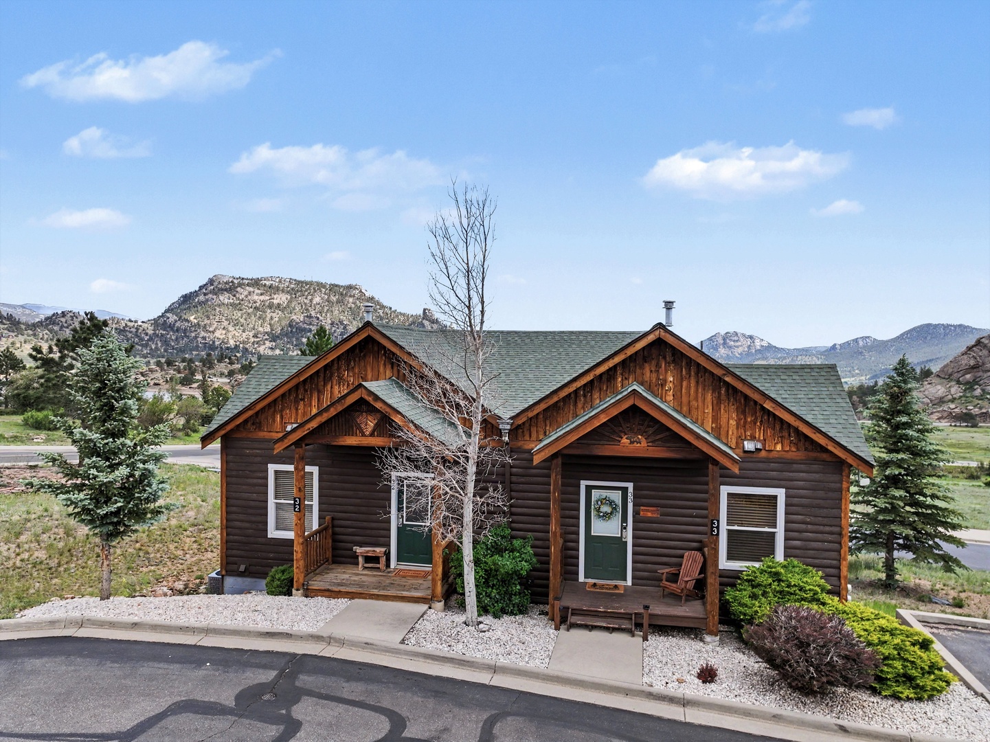 Charming home with wood siding and welcoming front porches, nestled in a scenic mountain valley with dramatic peaks in the distance.