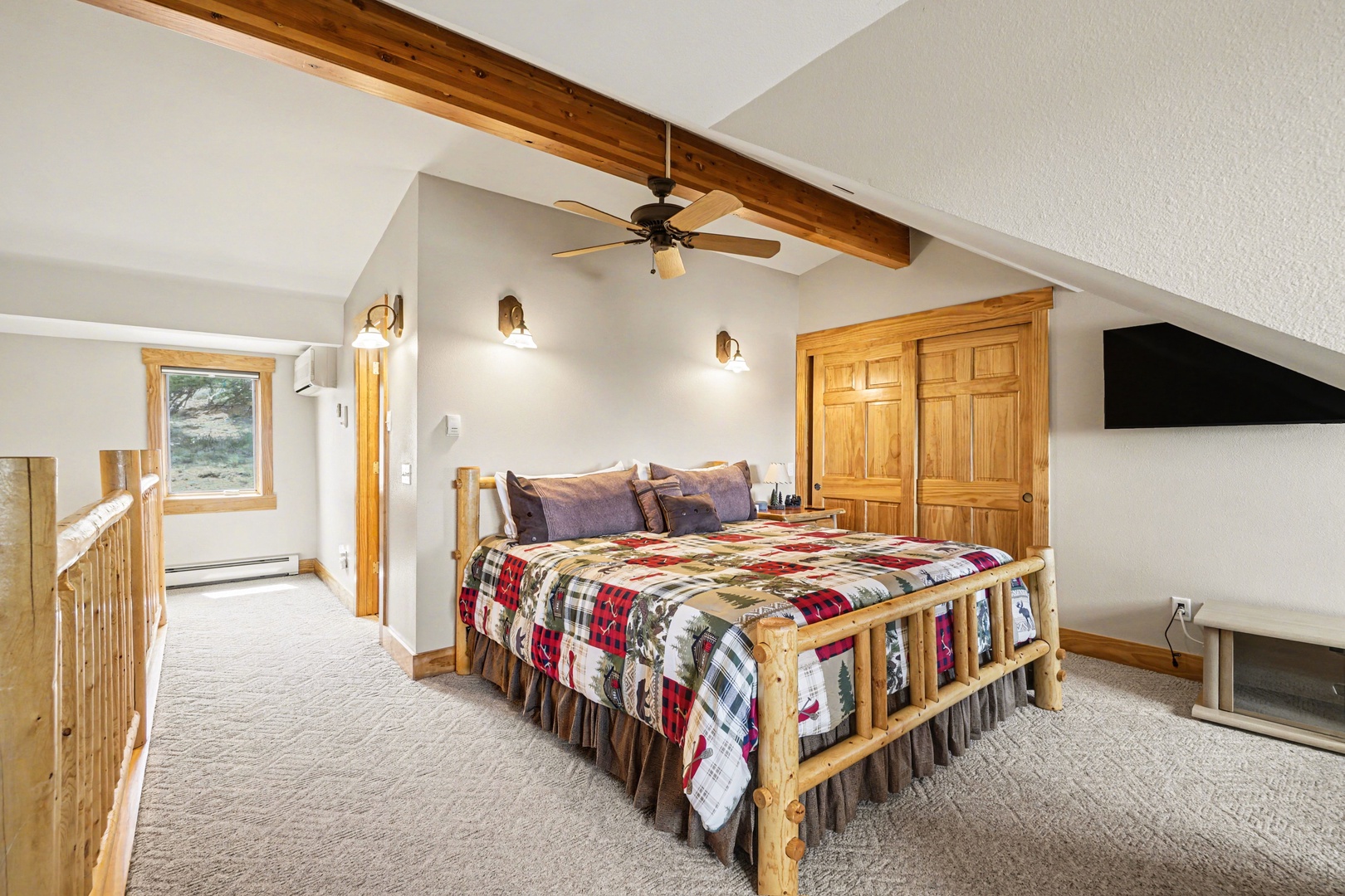 Rest peacefully in your cozy loft bedroom with rustic wood beams overhead and a colorful quilt that invites deep, restorative sleep.