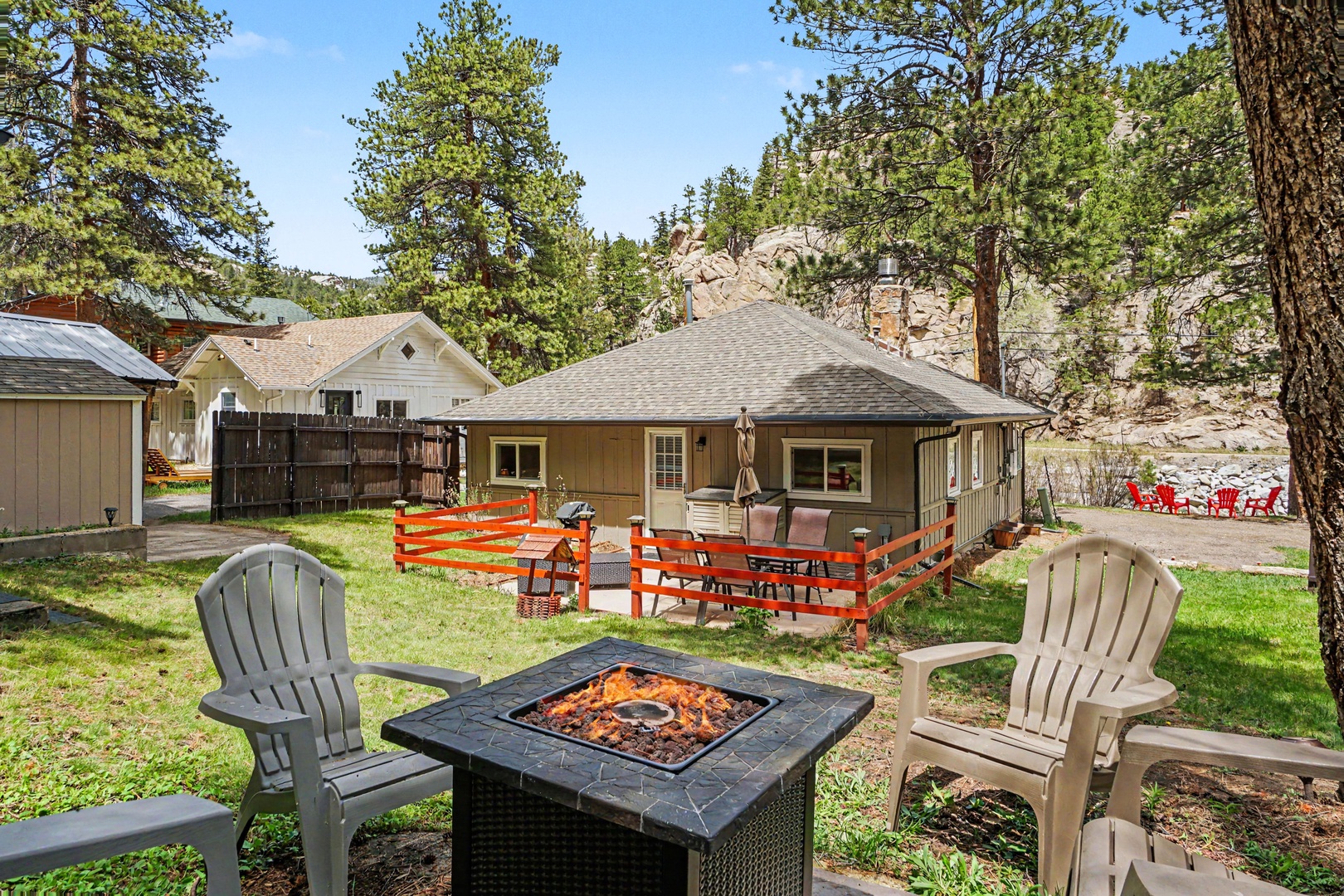 A vacation retreat where scenic mountain landscapes meet your private patio, complete with cozy fire pit seating and colorful red Adirondack chairs inviting relaxation under towering pine trees.