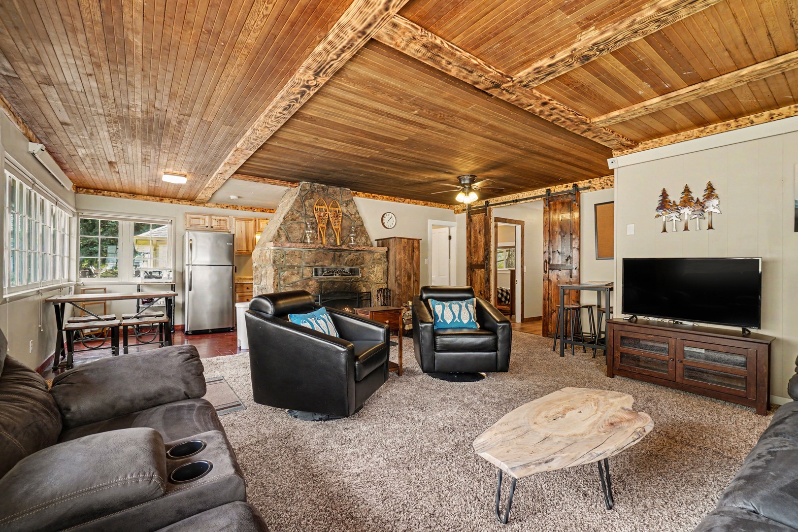 Relax in this cozy living room with vaulted wood ceilings, a stone fireplace, and plush seating. Your entertainment area includes a flat-screen TV, while the open layout connects you to the kitchen.