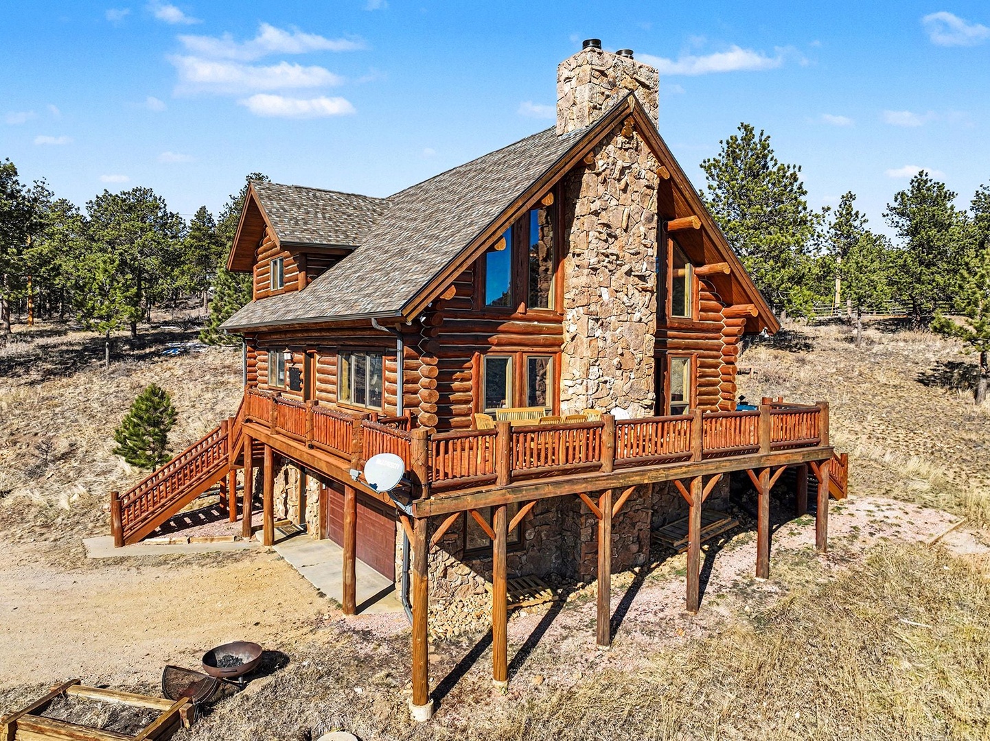 Mountain log cabin retreat with stone fireplace and wraparound deck nestled among pines and natural landscape.