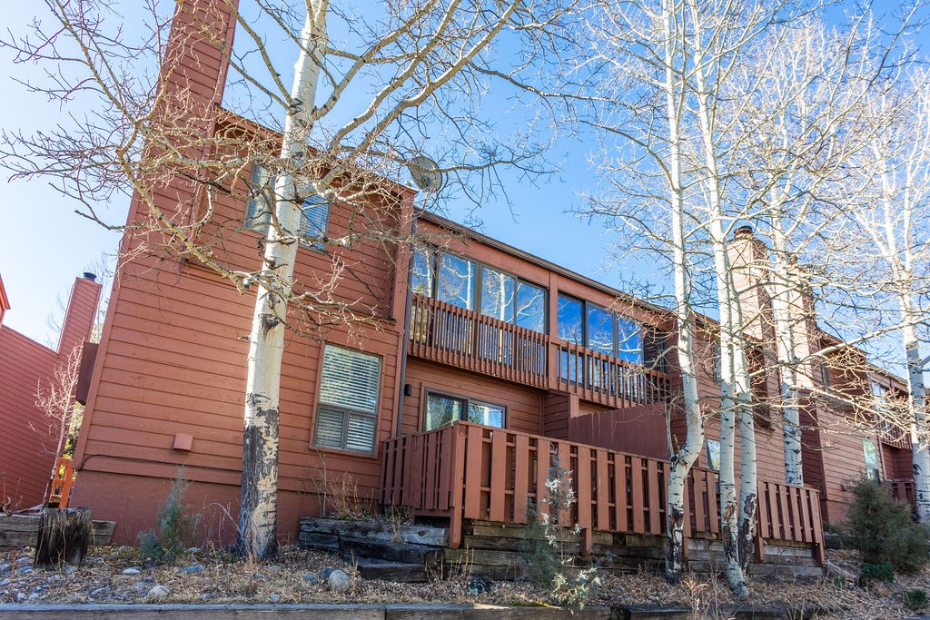 Charming mountain retreat with distinctive red-brown siding and multi-level balconies, nestled among bare aspen trees in a peaceful winter setting.