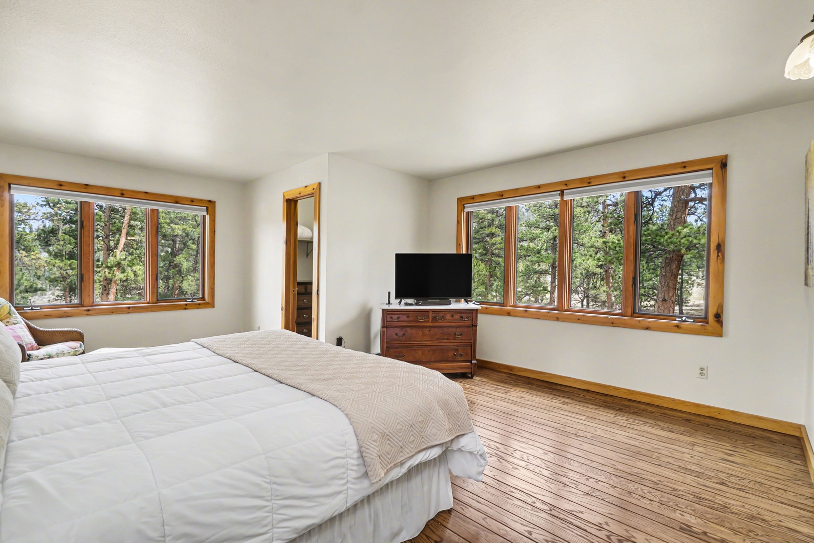 Wake up to forest views streaming through your bedroom's large windows, where warm wood floors and peaceful surroundings create your perfect retreat.