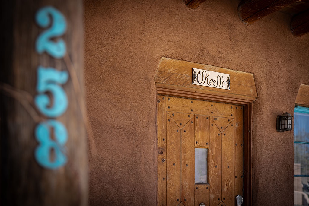 Adobe-style entrance with rustic wooden doors and charming property signage welcomes guests to this southwestern retreat.