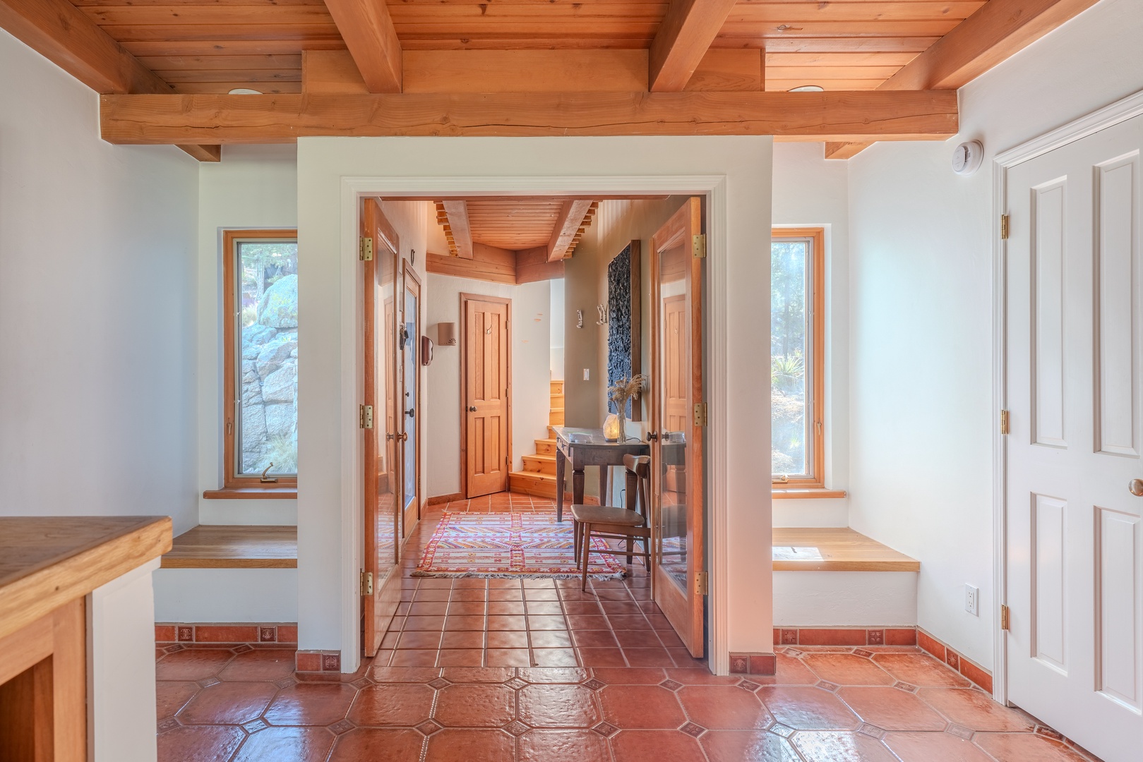 Warm terracotta tiles and exposed wood beams welcome you into this inviting entryway, where natural light streams through side windows, setting a cozy, Southwestern tone for your stay.