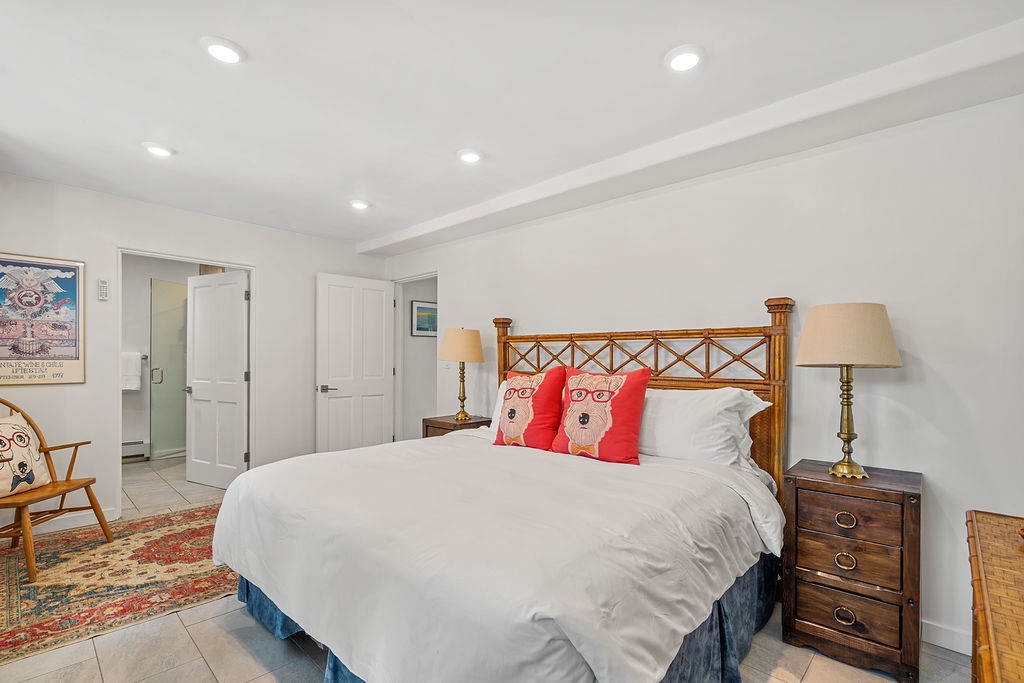 Sink into crisp white linens on your comfortable bed, surrounded by warm wood furnishings and charming coastal decor in this bright, welcoming bedroom.