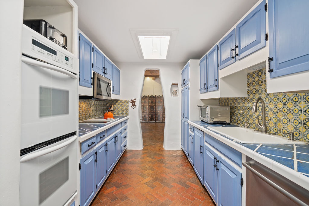Your stunning blue galley kitchen features vibrant tile backsplash, stainless appliances, and terracotta floors for Mediterranean charm.