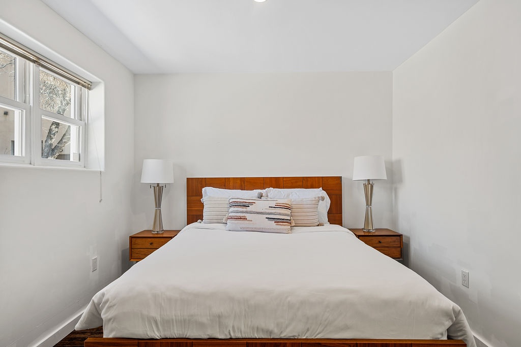 Sink into crisp white linens in your serene bedroom, where warm wood tones and soft lighting create the perfect retreat for restful nights.