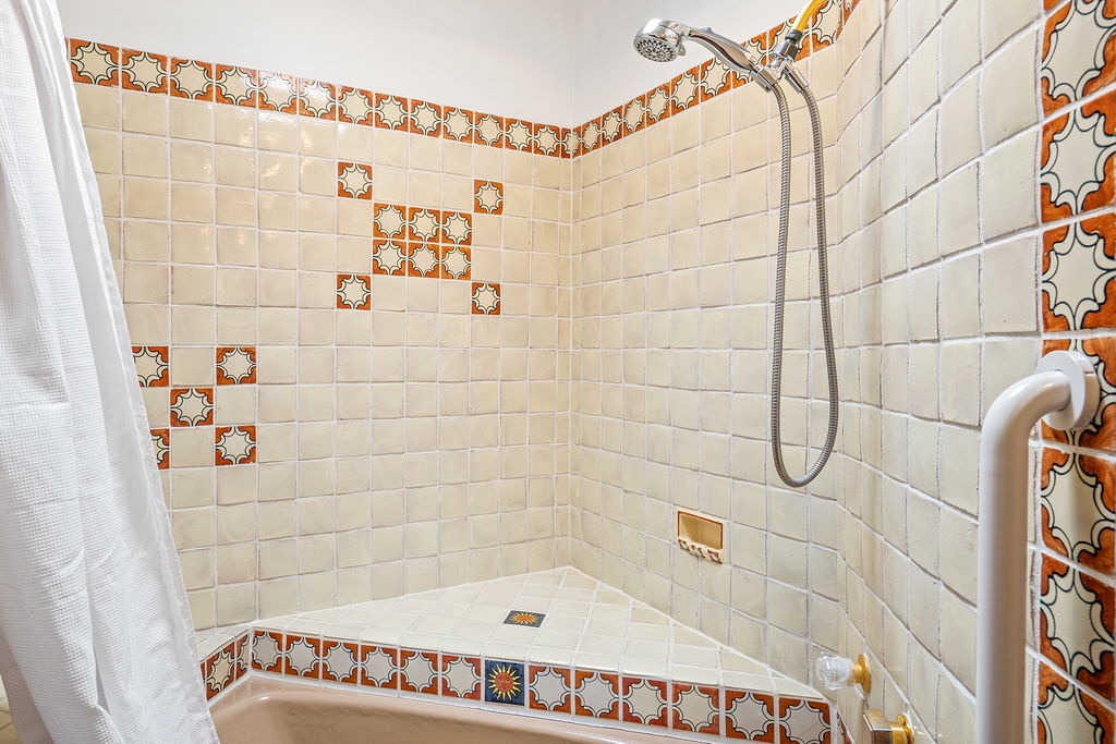Step into your beautifully tiled shower with charming terracotta accents and handheld showerhead for a refreshing start to your morning.