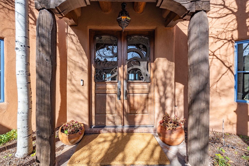 Warm adobe walls and elegant wrought iron doors create an inviting Southwest entrance, framed by natural wood beams and decorative pottery.