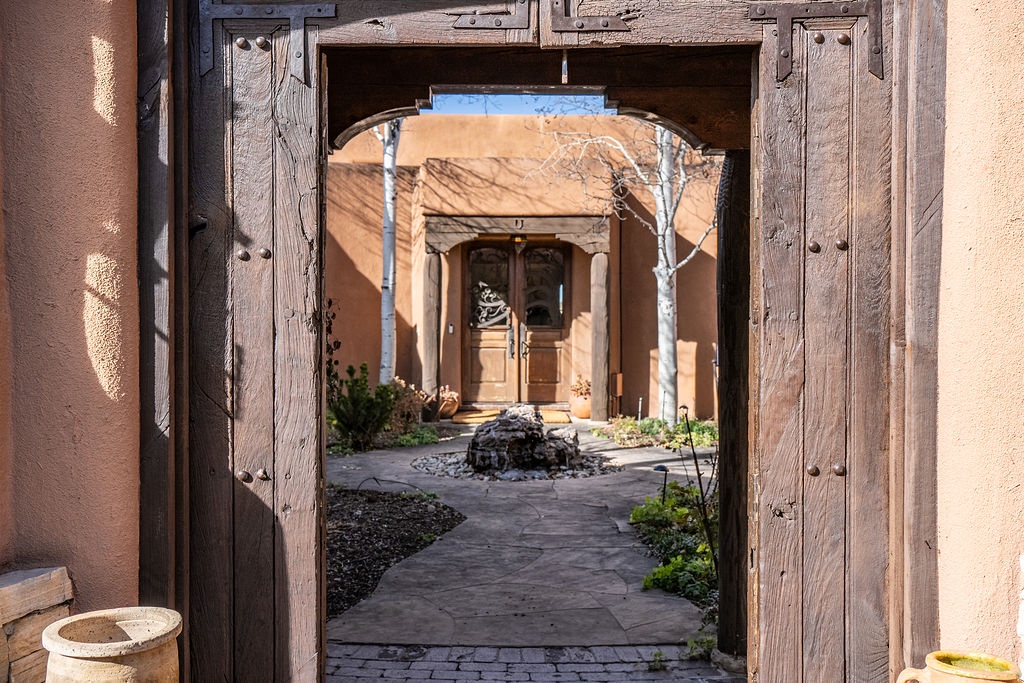 A rustic wooden gate frames the entrance to an enchanting inner courtyard with stone pathways and desert landscaping.