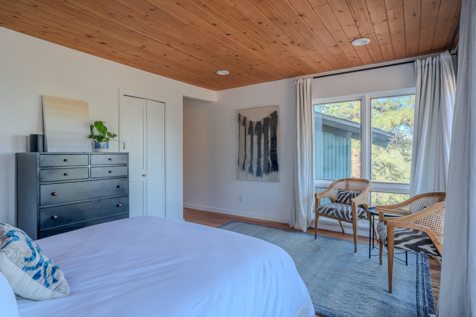 Drift off in your serene bedroom, where warm wood ceilings meet crisp linens and a cozy seating nook by the window invites morning coffee or quiet contemplation.