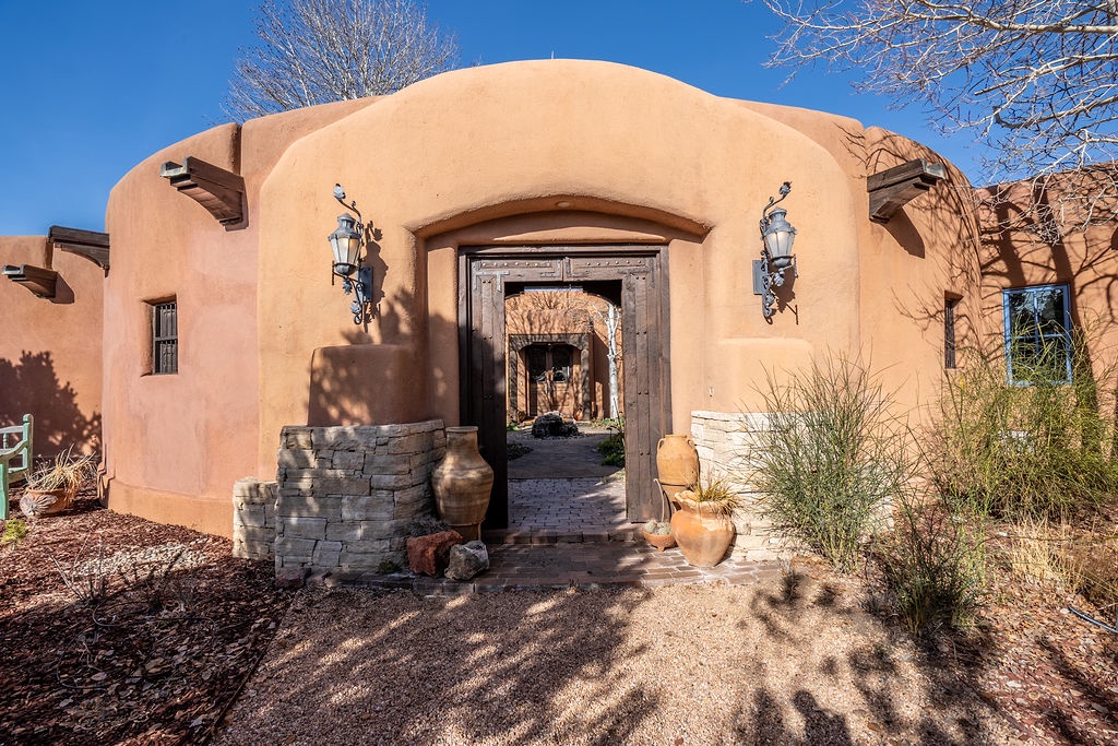 Adobe-style property entrance with rustic wooden doors, decorative lanterns, and desert landscaping beneath clear blue skies.