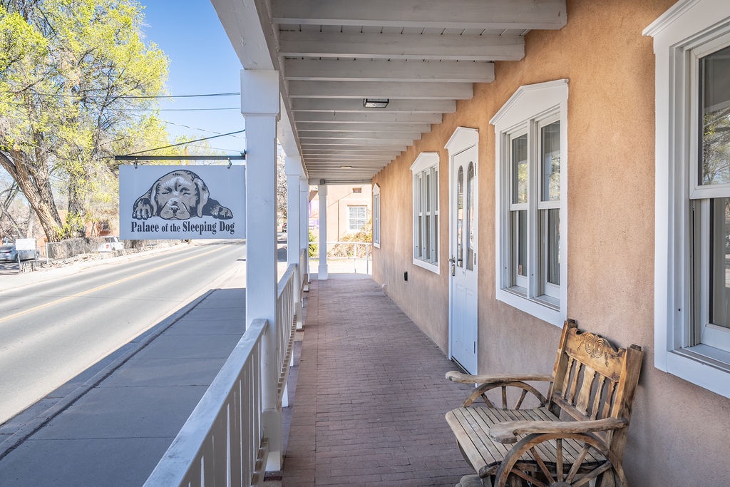Historic adobe building with covered walkway and wooden benches offers a charming entrance to the Palace of the Sleeping Dog establishment.