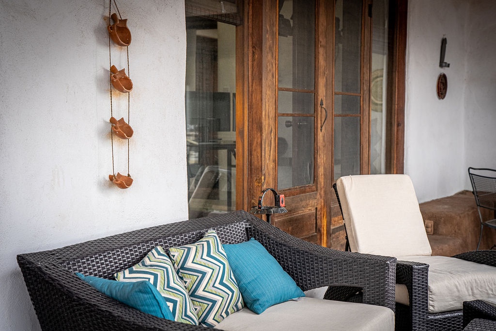 Settle into comfortable wicker seating with vibrant pillows on your private terrace, where warm wood and thoughtful decor create the perfect outdoor retreat.