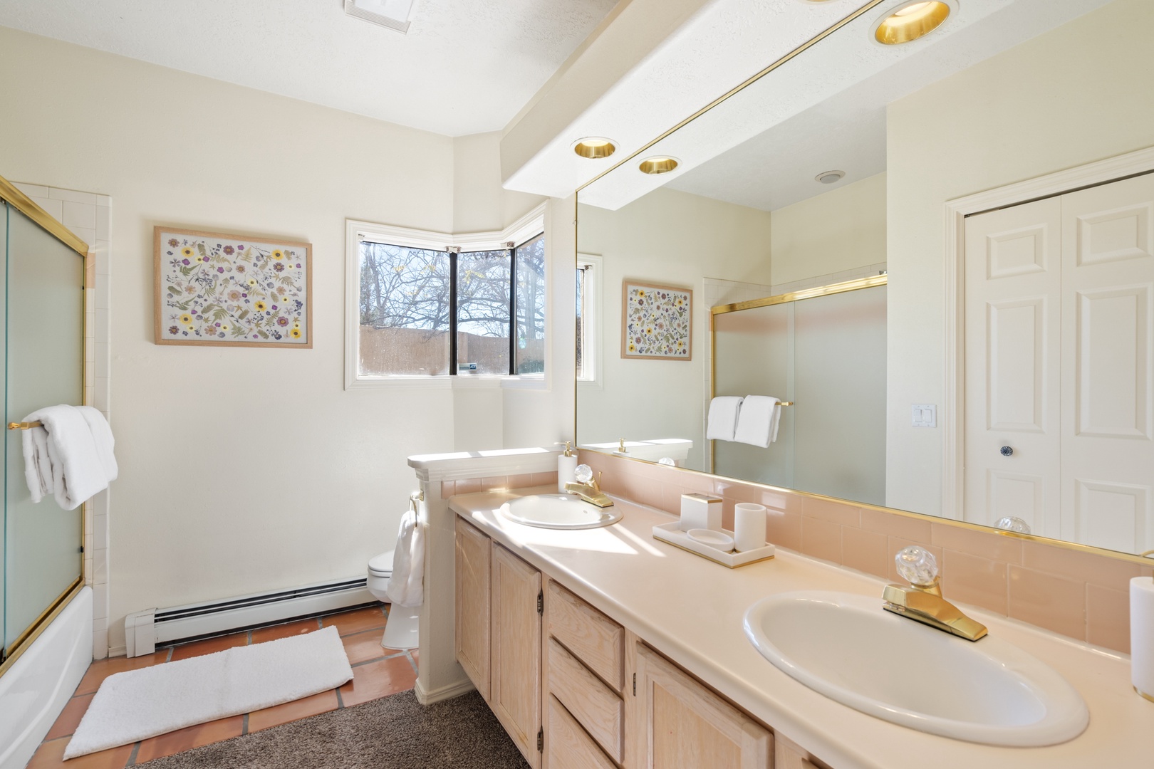 Unwind in your spacious bathroom featuring dual sinks, elegant gold fixtures, and soft natural light streaming through the window