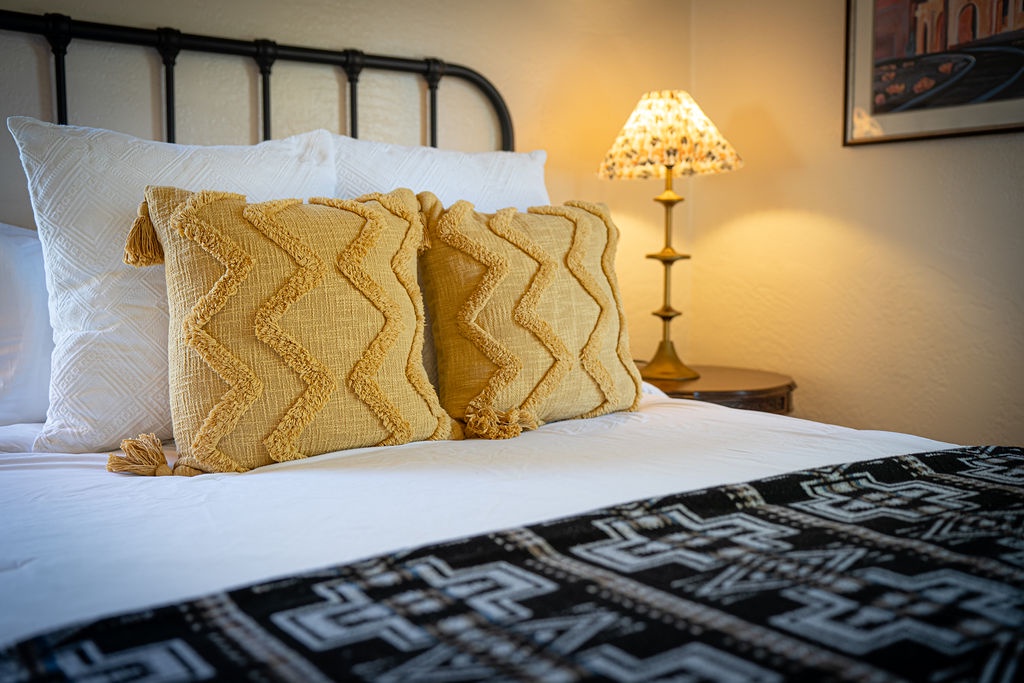 Sink into crisp white linens and textured golden pillows as warm lamplight creates your perfect evening sanctuary.