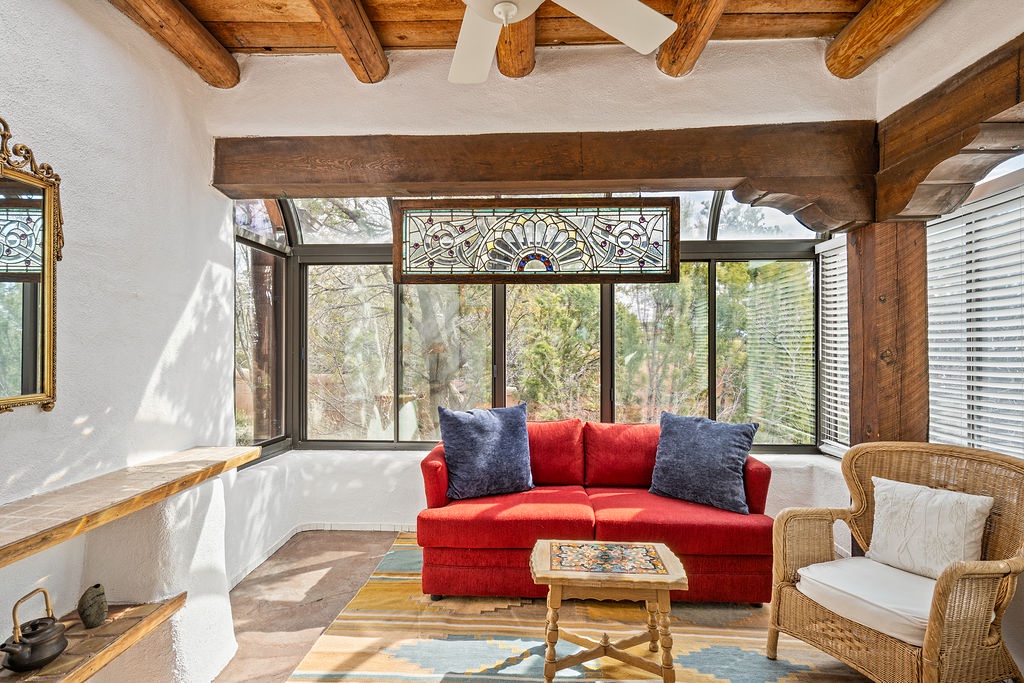 Relax in this charming living room where rustic wooden beams meet vibrant red furnishings, all bathed in natural light from panoramic windows.
