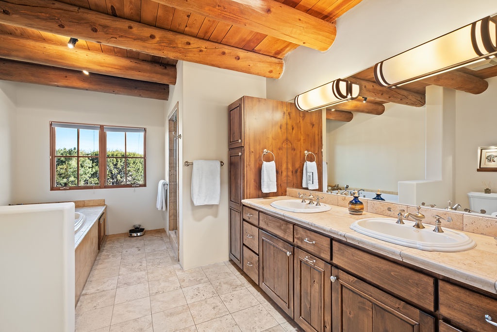 Soak in your private spa-like bathroom featuring exposed wooden beams, dual vanities, and a deep soaking tub with garden views.