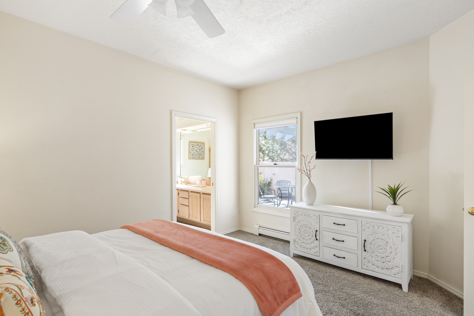 Unwind in your spacious bedroom featuring a wall-mounted TV and elegant white dresser, with an ensuite bathroom just steps away for your convenience.