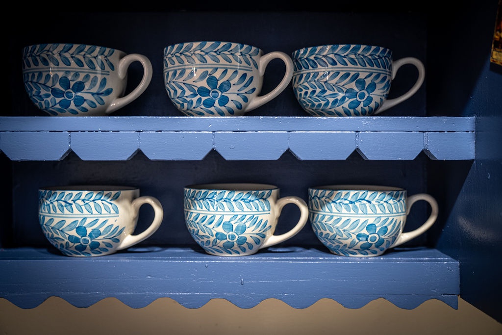 Handcrafted blue ceramic teacups await your morning brew on charming rustic shelves.