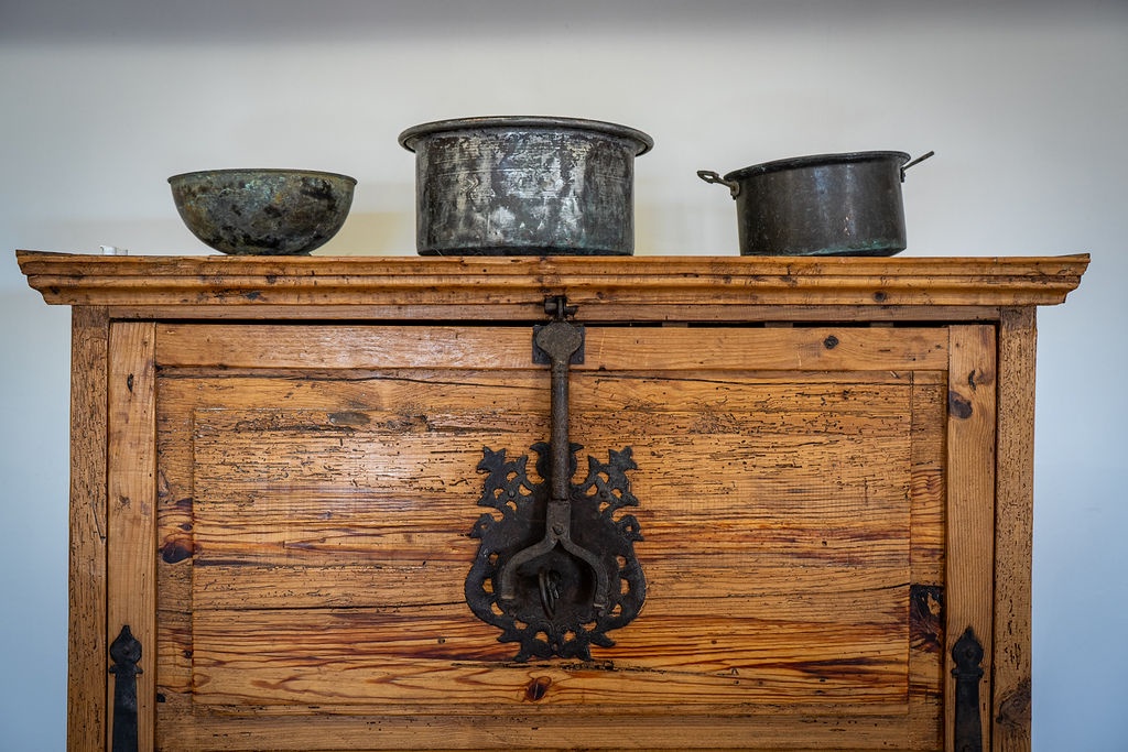 Vintage wooden cabinet topped with weathered metal pots creates authentic rustic charm in your kitchen space.