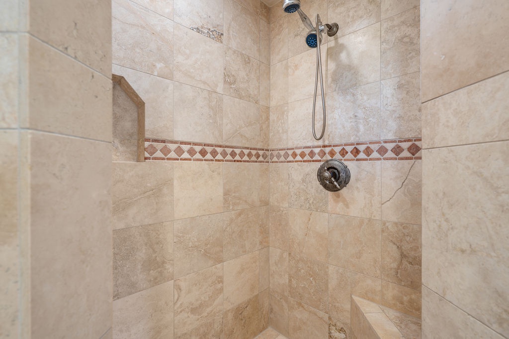 Step into your luxurious travertine shower with dual rainfall heads and handheld sprayer for the ultimate refreshing experience.