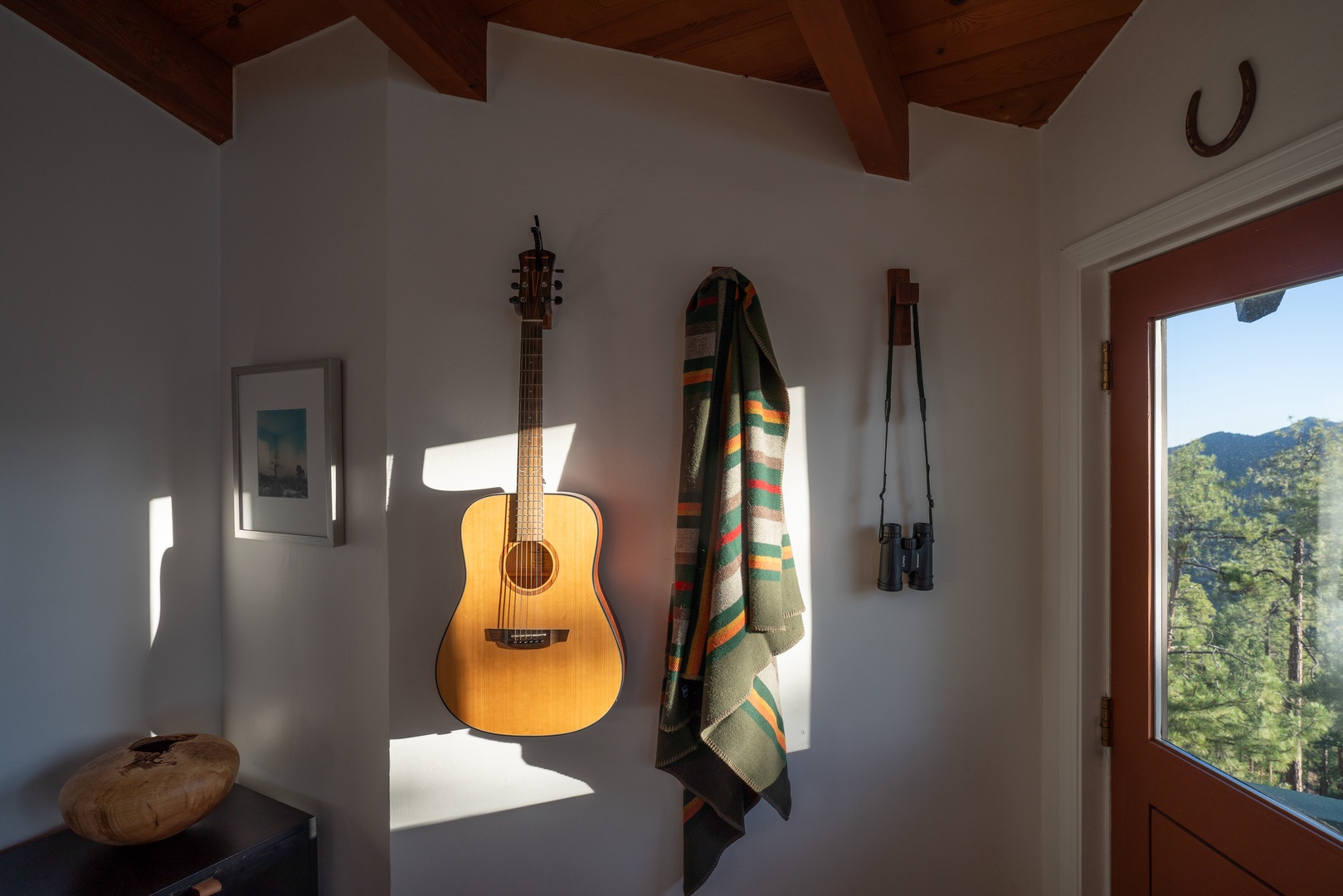 Step inside your mountain retreat where rustic charm meets creative comfort. Warm wooden beams frame your personal sanctuary, while sunlight filters through the doorway, revealing stunning forest and mountain vistas just beyond.