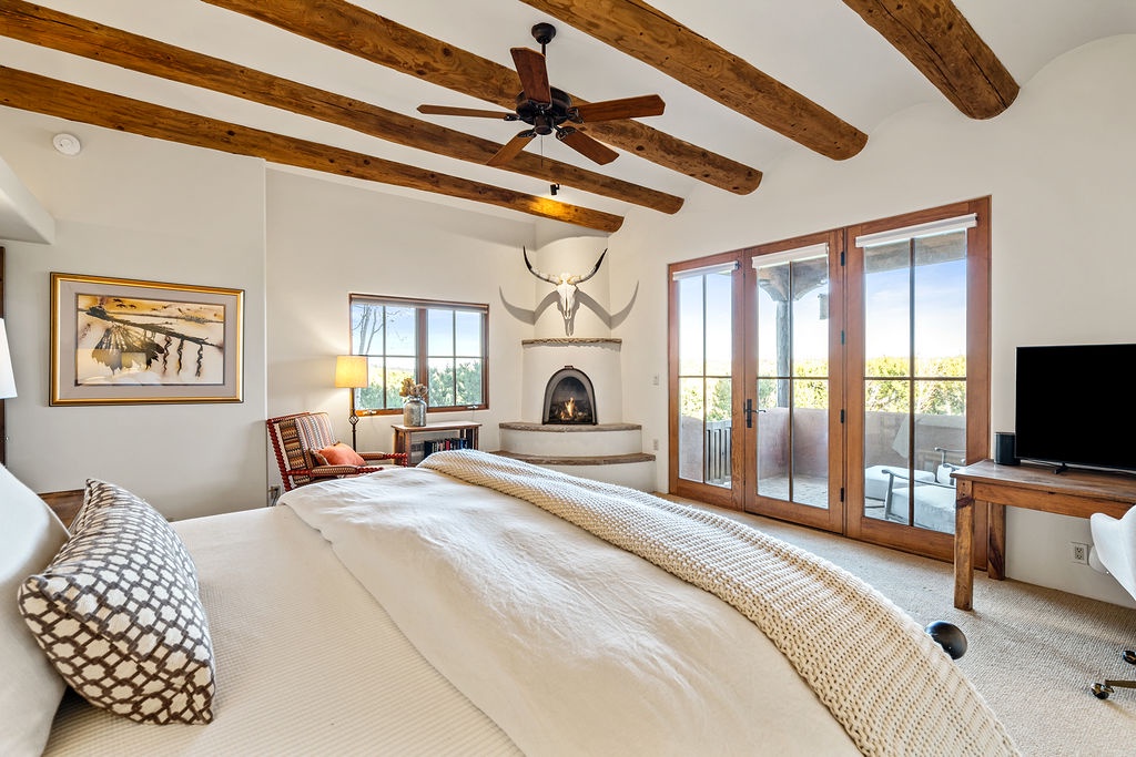 Unwind in your spacious bedroom featuring exposed wood beams, a cozy corner fireplace, and private balcony access for peaceful moments.