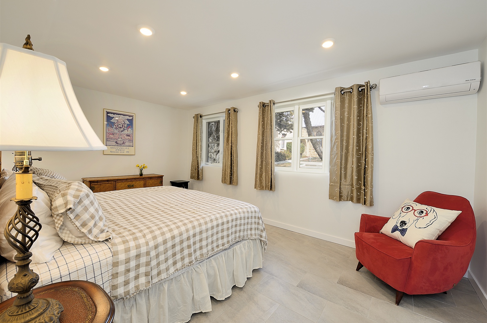 Unwind in your bright bedroom featuring plaid bedding, cozy red accent chair, and peaceful atmosphere perfect for restful nights.