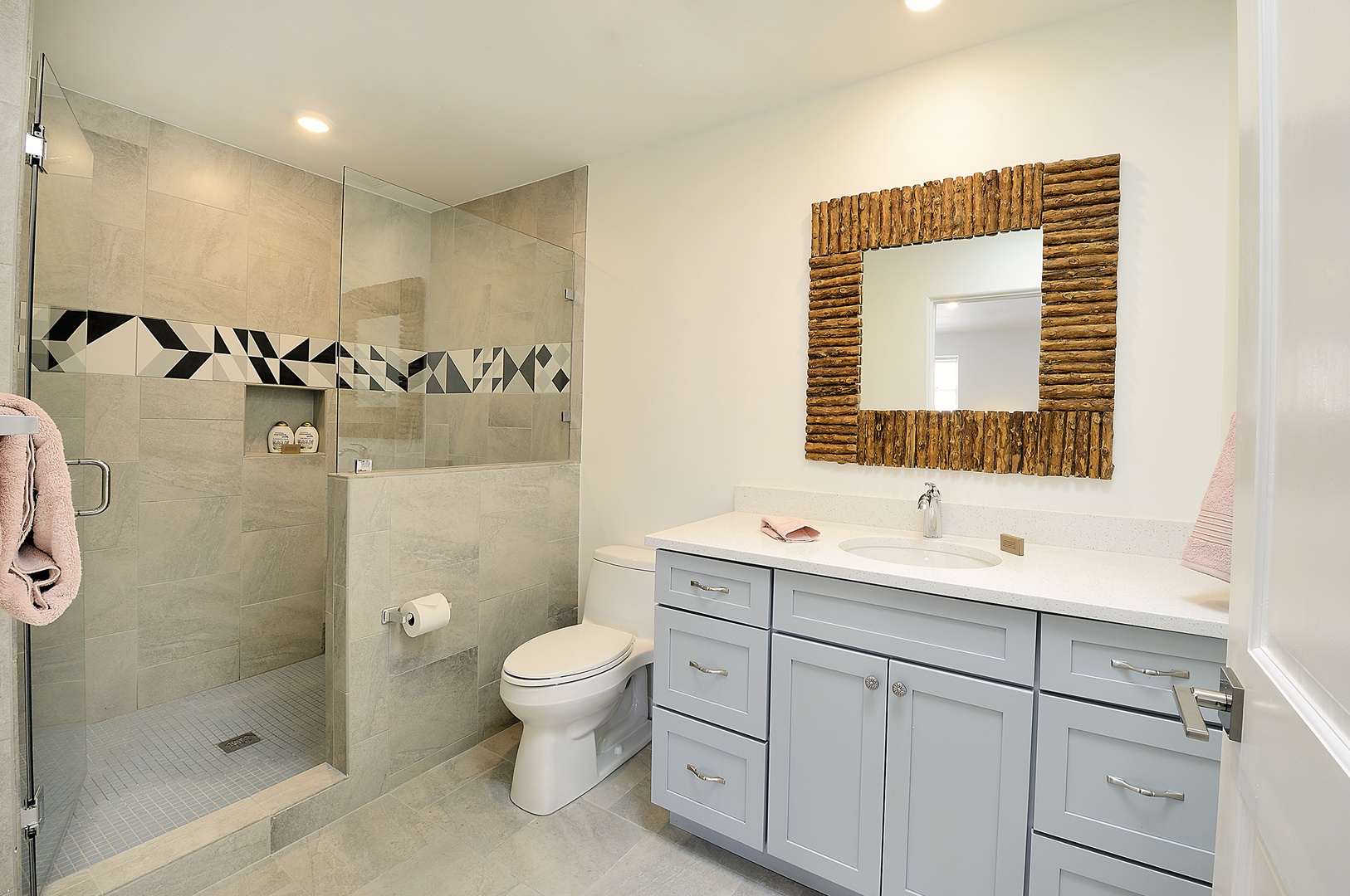 Step into your spa-like bathroom with its sleek walk-in shower, stylish geometric tile accents, and beautiful natural wood mirror frame.