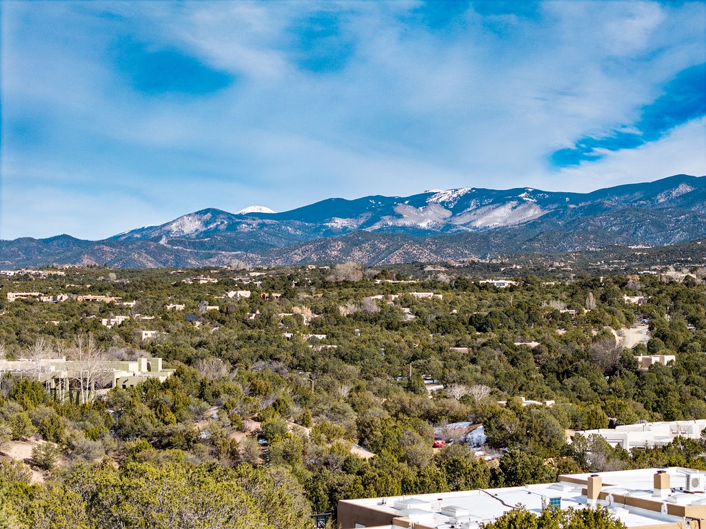 Stunning mountain landscape with snow-capped peaks rising above a tree-lined valley dotted with residential properties.