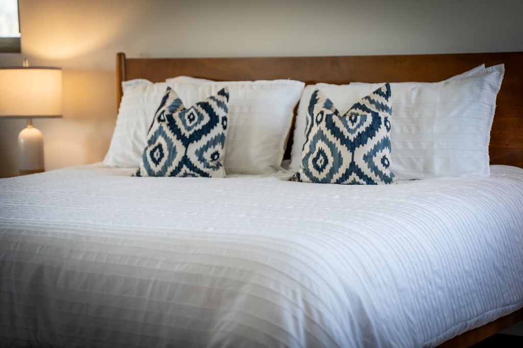 Sink into crisp white linens and stylish blue patterned pillows in your comfortable bedroom retreat, perfectly lit for restful nights.