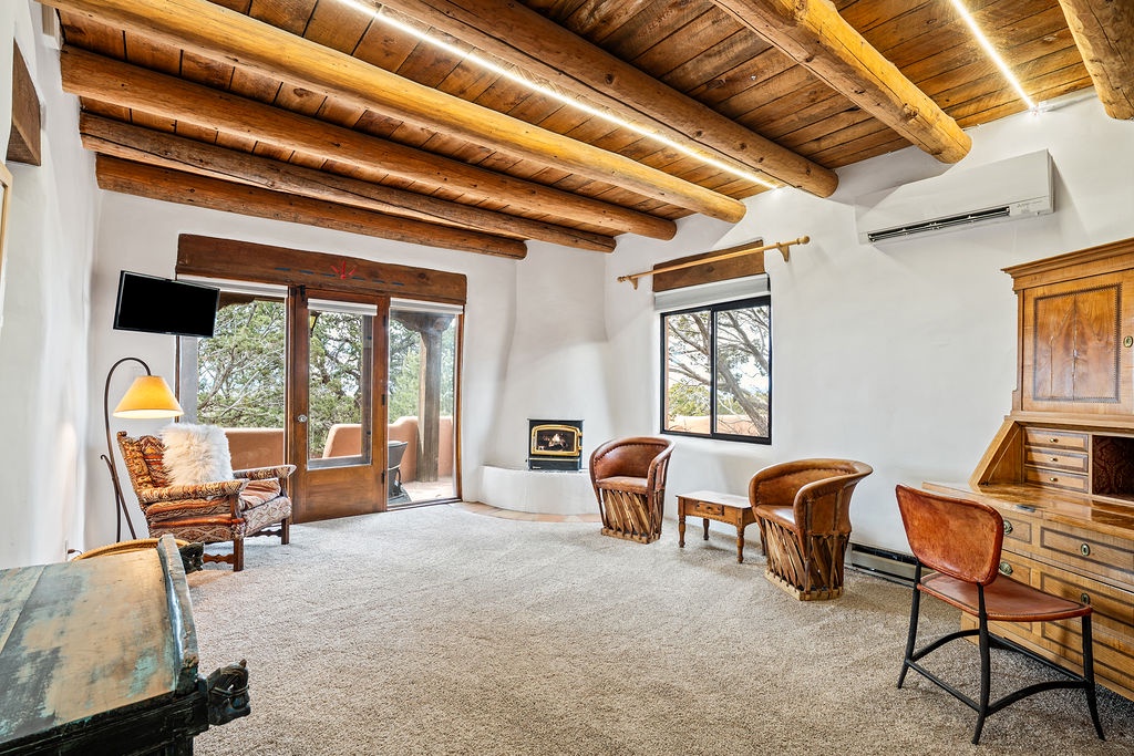 Relax in your spacious living room featuring beautiful exposed wooden beams, warm leather seating, and peaceful garden views through French doors.