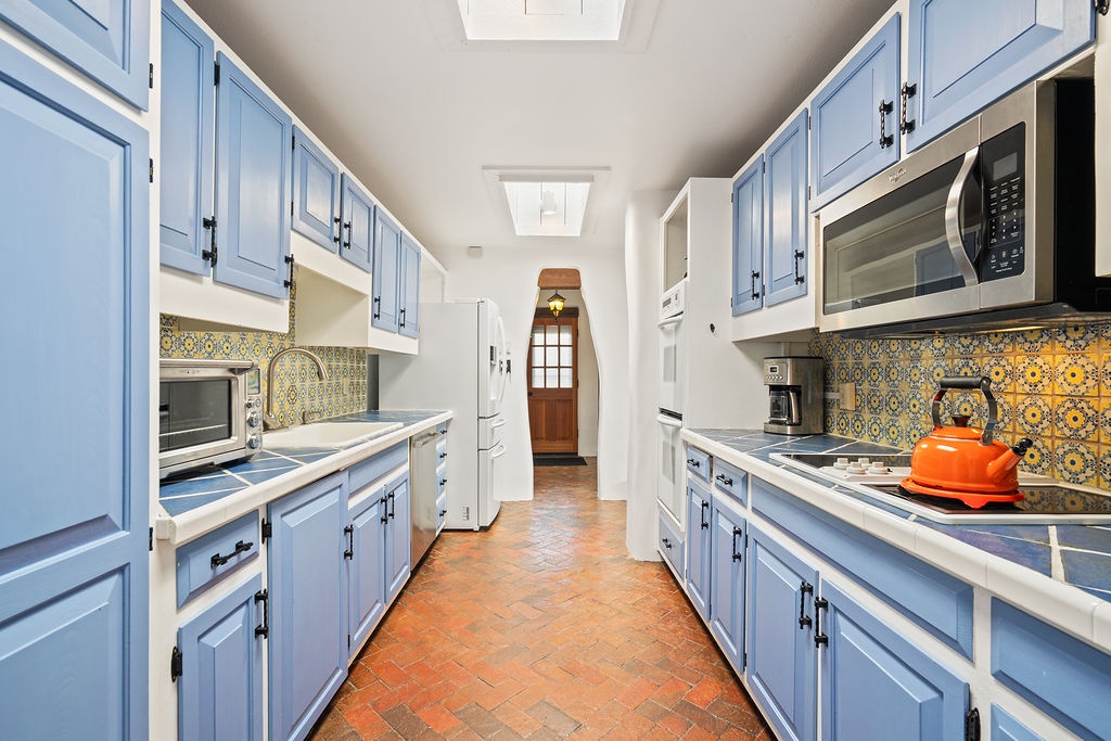 Step into your fully equipped galley kitchen with charming blue cabinets, colorful tile backsplash, and everything you need to cook memorable meals.