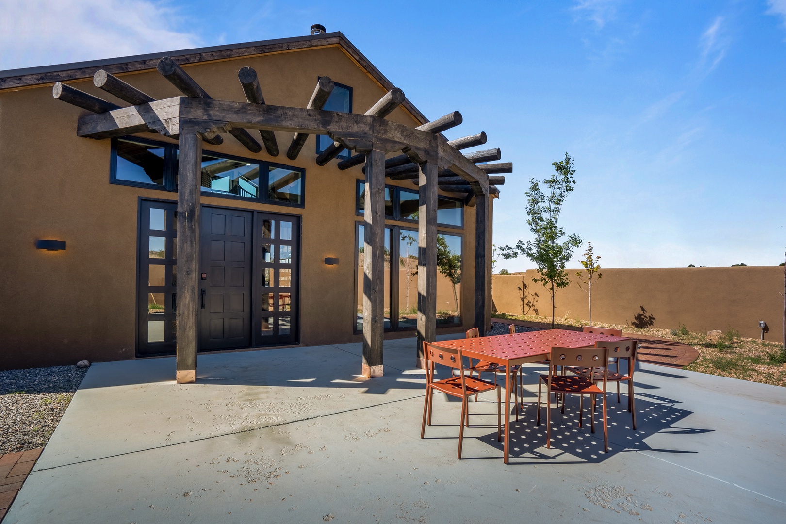 Modern southwestern-style property with striking wooden pergola entrance and private outdoor dining space under expansive blue skies.