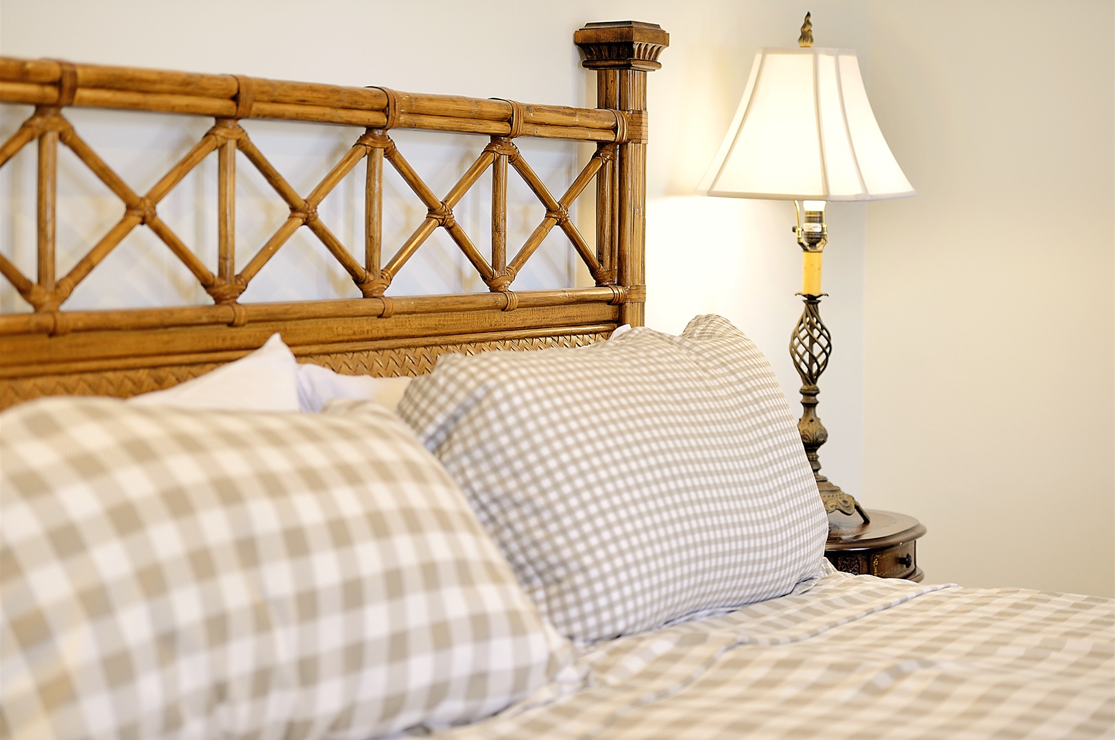 Sink into your cozy bed with elegant bamboo headboard and soft gingham linens, perfect for peaceful nights under gentle lamplight.