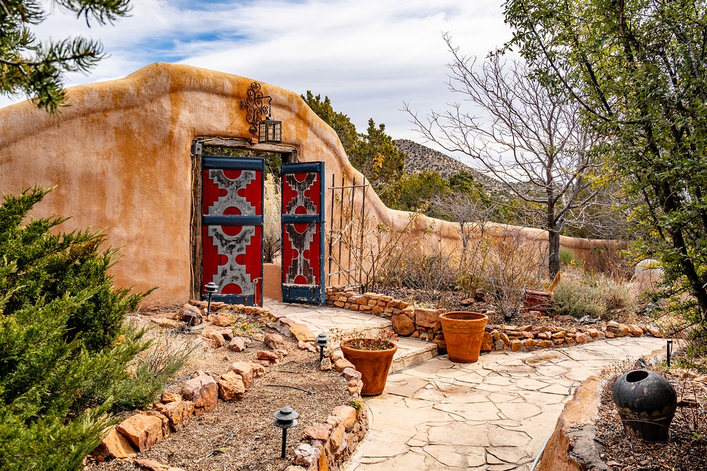 Adobe-style entrance with colorful doors, surrounded by native plants and mountain views creating an authentic southwestern arrival experience.
