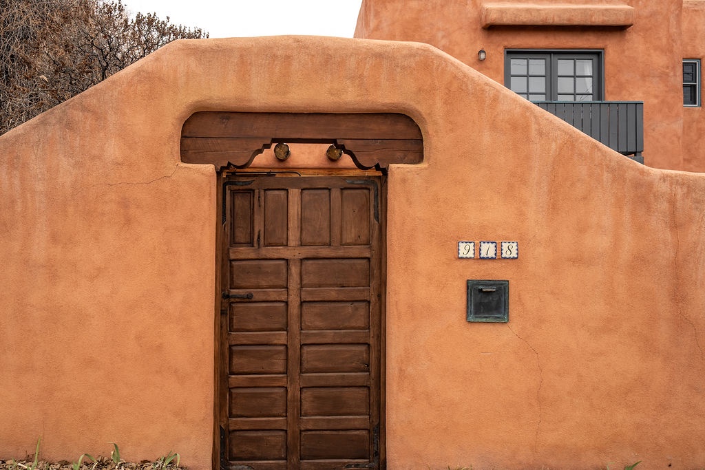 Traditional adobe architecture with characteristic curved walls and wooden door creates an authentic southwestern entrance experience.