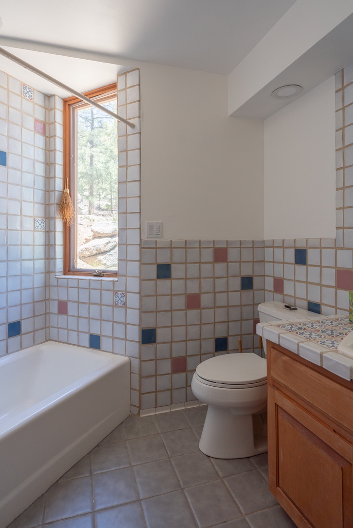 Bright, airy bathroom with playful tile accents in pink and blue, a soaking tub, and woodland views from your window, creating a serene escape.