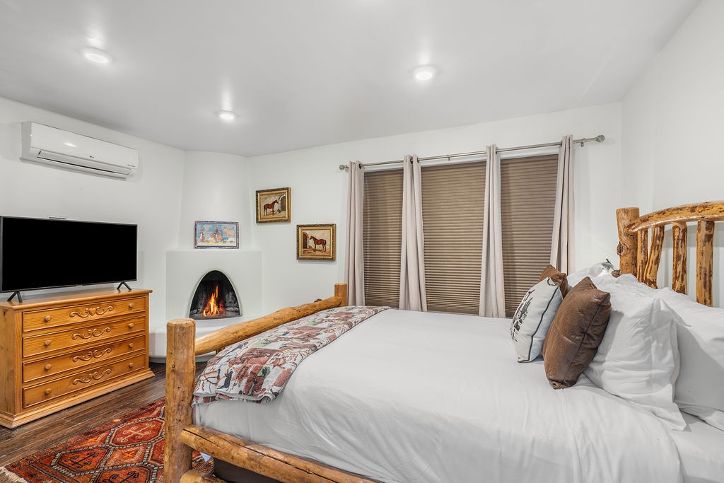Unwind in your cozy bedroom with rustic log bed, crackling fireplace, and modern comforts like AC and TV for perfect relaxation.