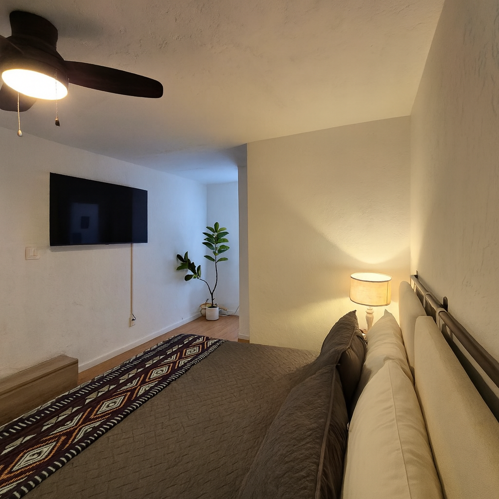 Unwind in your cozy bedroom featuring soft ambient lighting, a wall-mounted TV for entertainment, and thoughtful touches like a decorative plant to create a relaxing atmosphere.