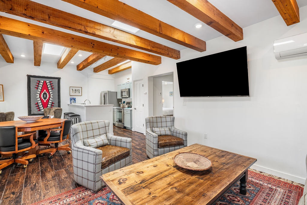 Relax under rustic wooden beams in your stylish living space, featuring comfortable seating and a large TV for cozy evenings in.