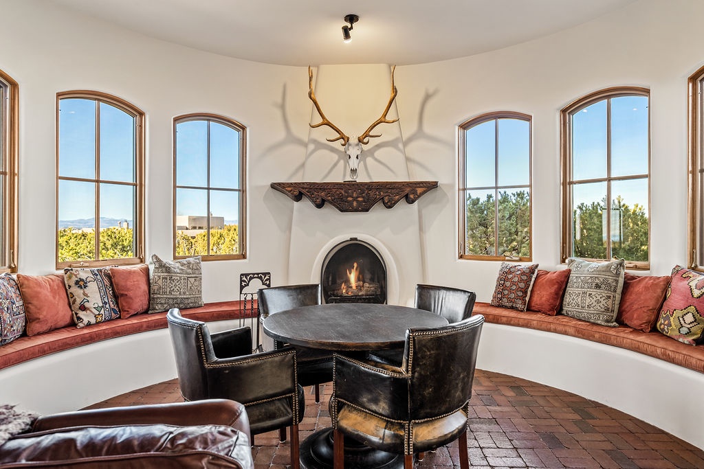 Gather around the crackling fireplace in your elegant dining nook, where rustic antlers and colorful cushions create the perfect atmosphere for memorable meals.